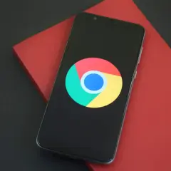 Smartfon z logo Google Chrome na czarnym ekranie, leżący na czerwonym tle.