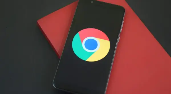 Smartfon z logo Google Chrome na czarnym ekranie, leżący na czerwonym tle.