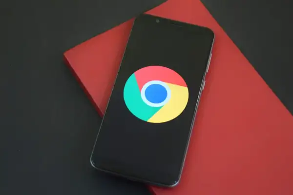 Smartfon z logo Google Chrome na czarnym ekranie, leżący na czerwonym tle.